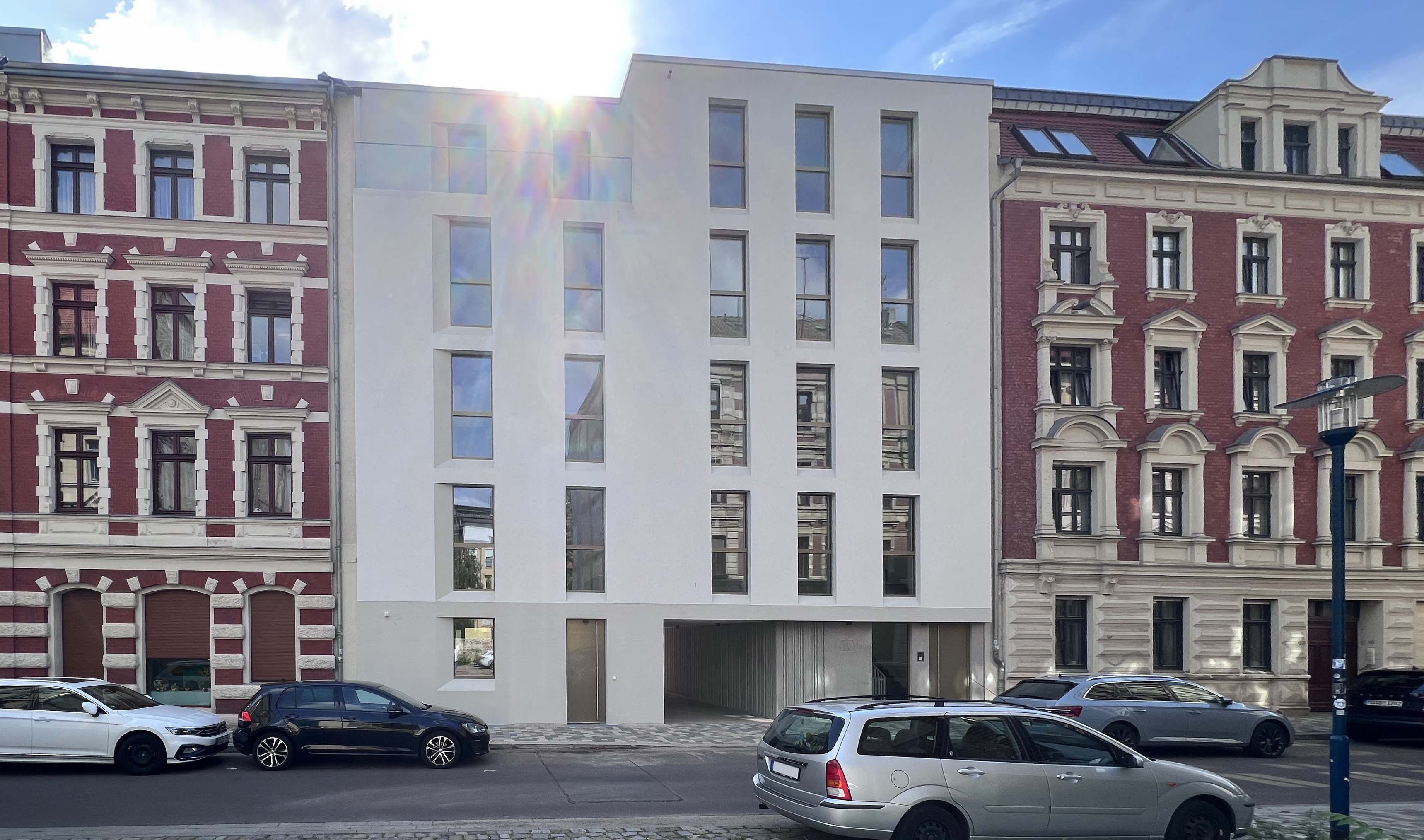 Moderne Stadtfassade mit klarer Architektur zwischen zwei Altbauten, zentral gelegen mit Tiefgaragenzufahrt und großen Fenstern.