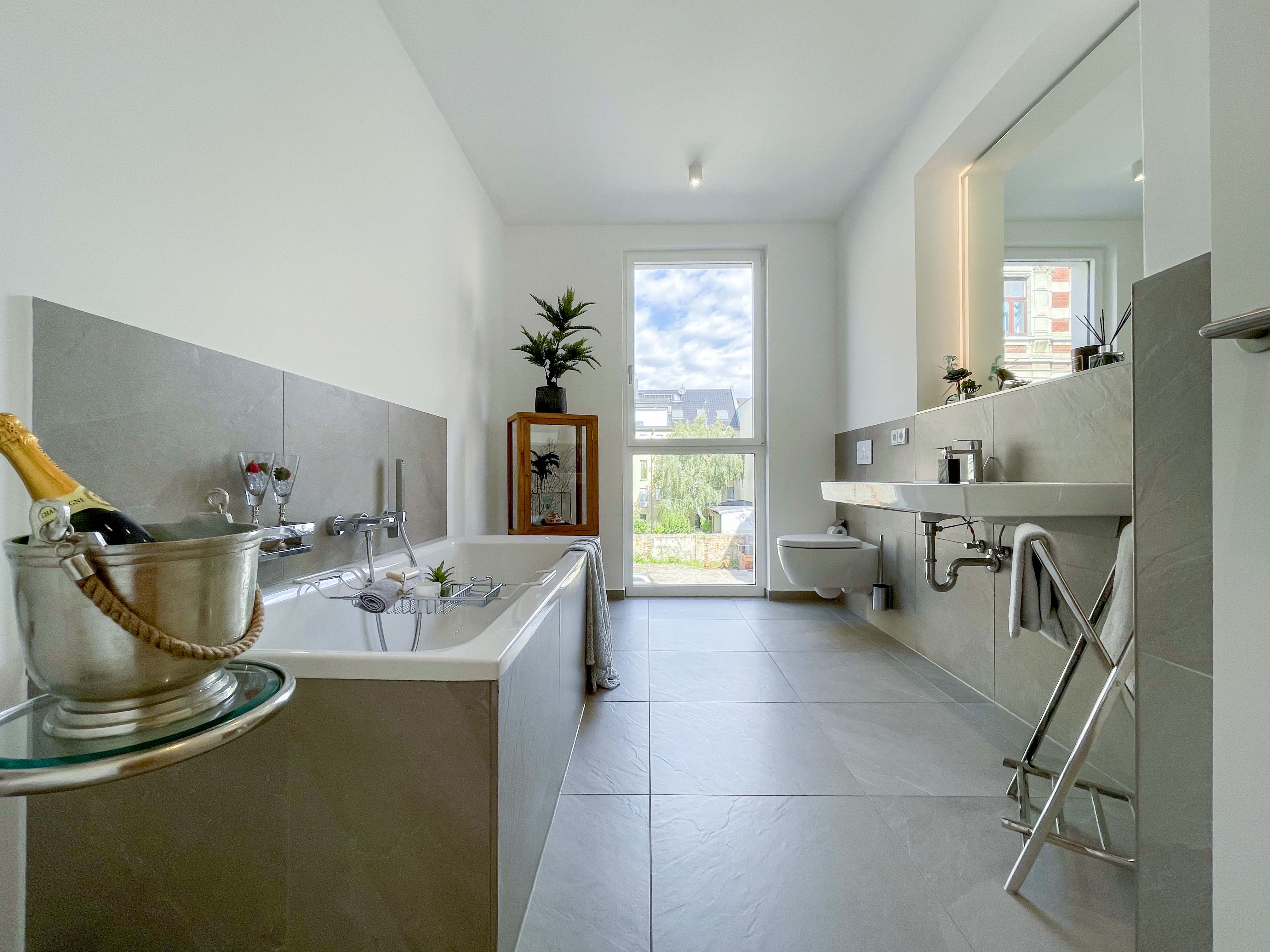 Modernes, helles Badezimmer mit Badewanne, bodentiefem Fenster, stilvollen Fliesen und hochwertiger Ausstattung.